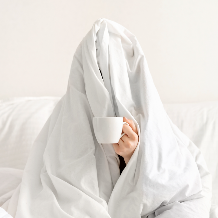 a person with a white cup under a blanket