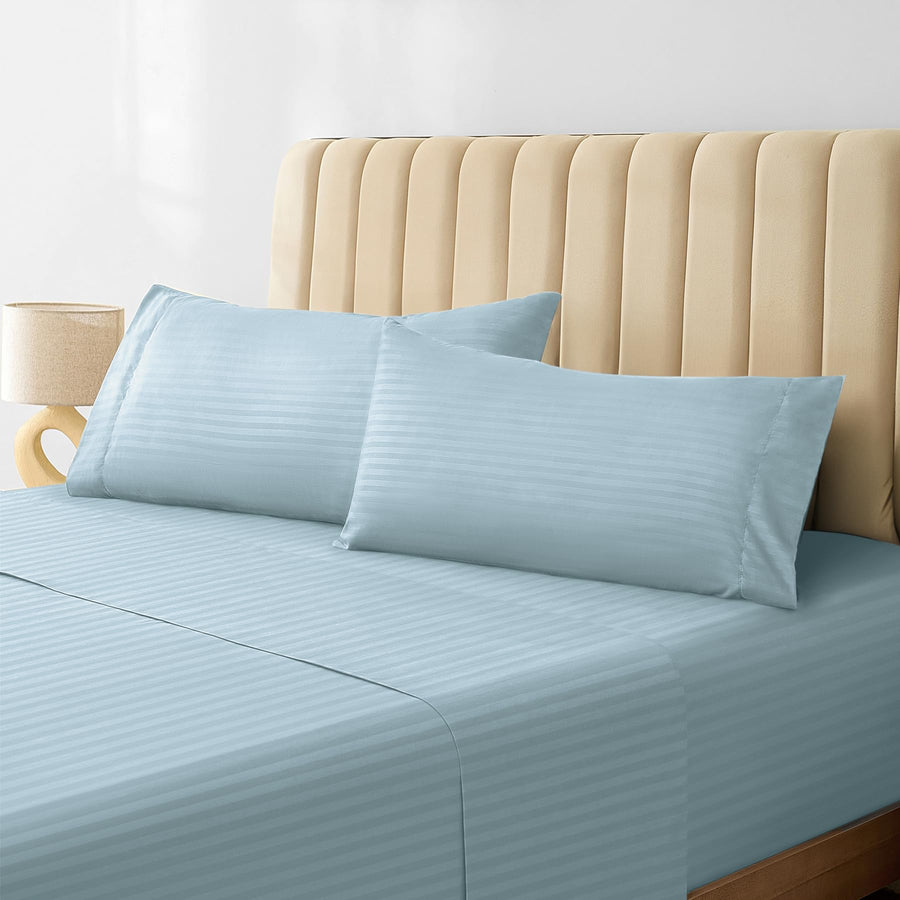 a bed with a light blue sheet and a tan headboard